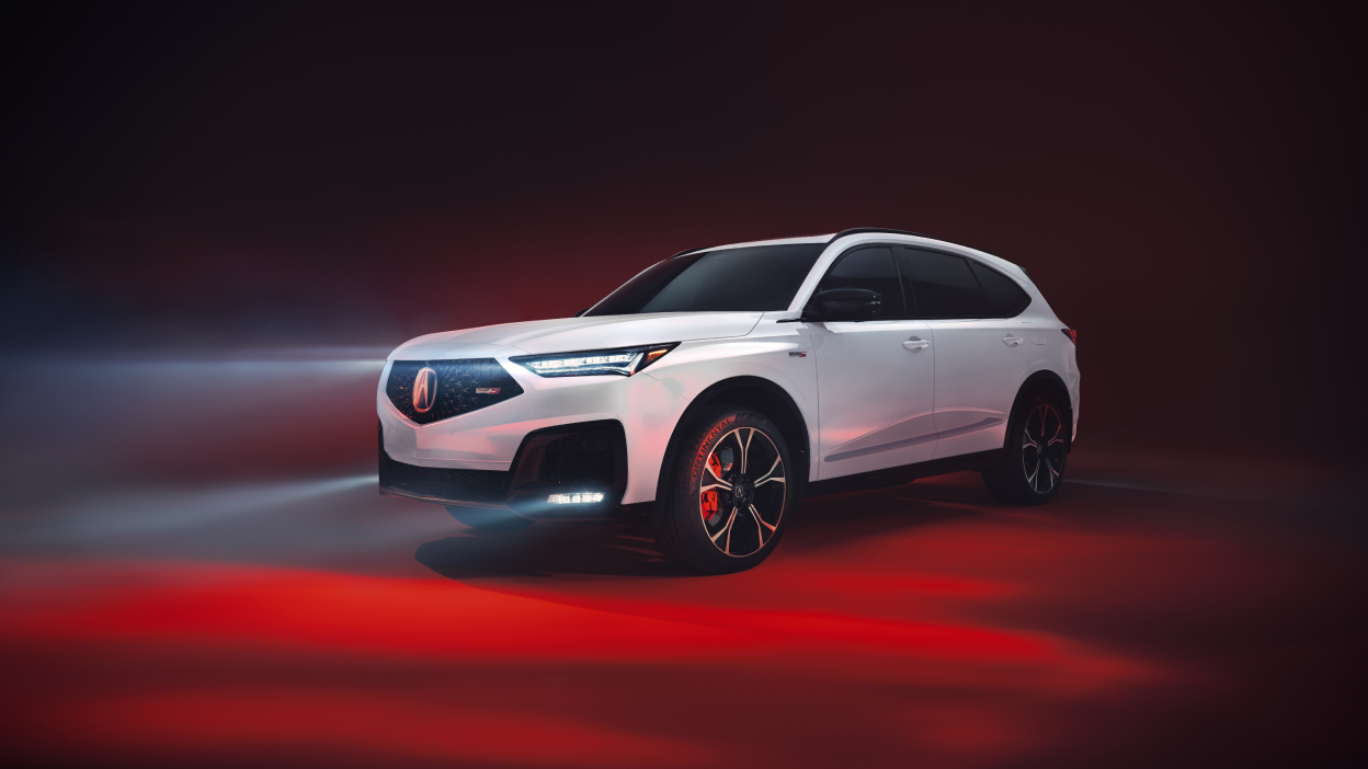 A red MDX drives down a road in the wilderness.